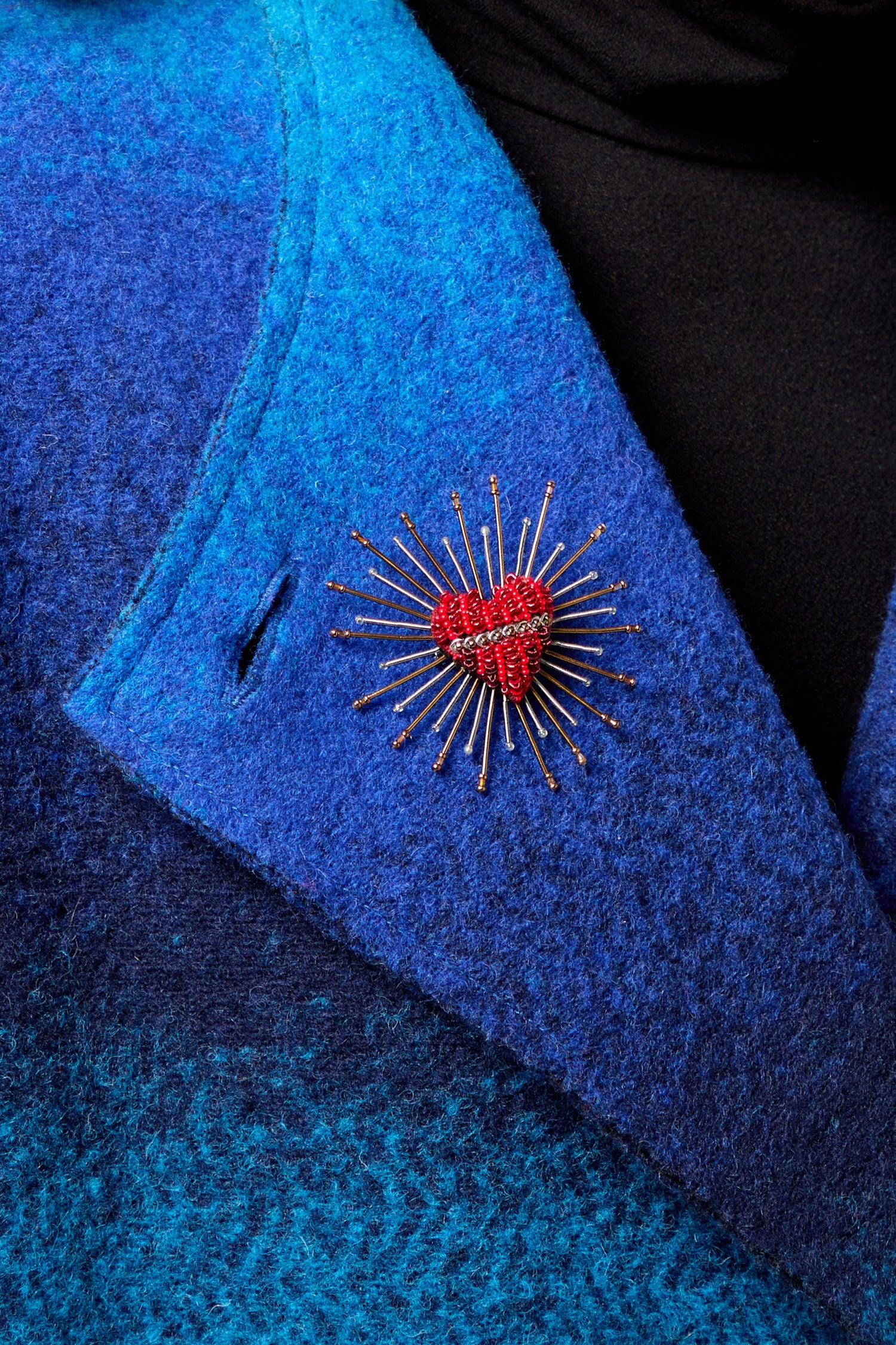 A blue coat with a Sacred Heart Embroidered Brooch on it.