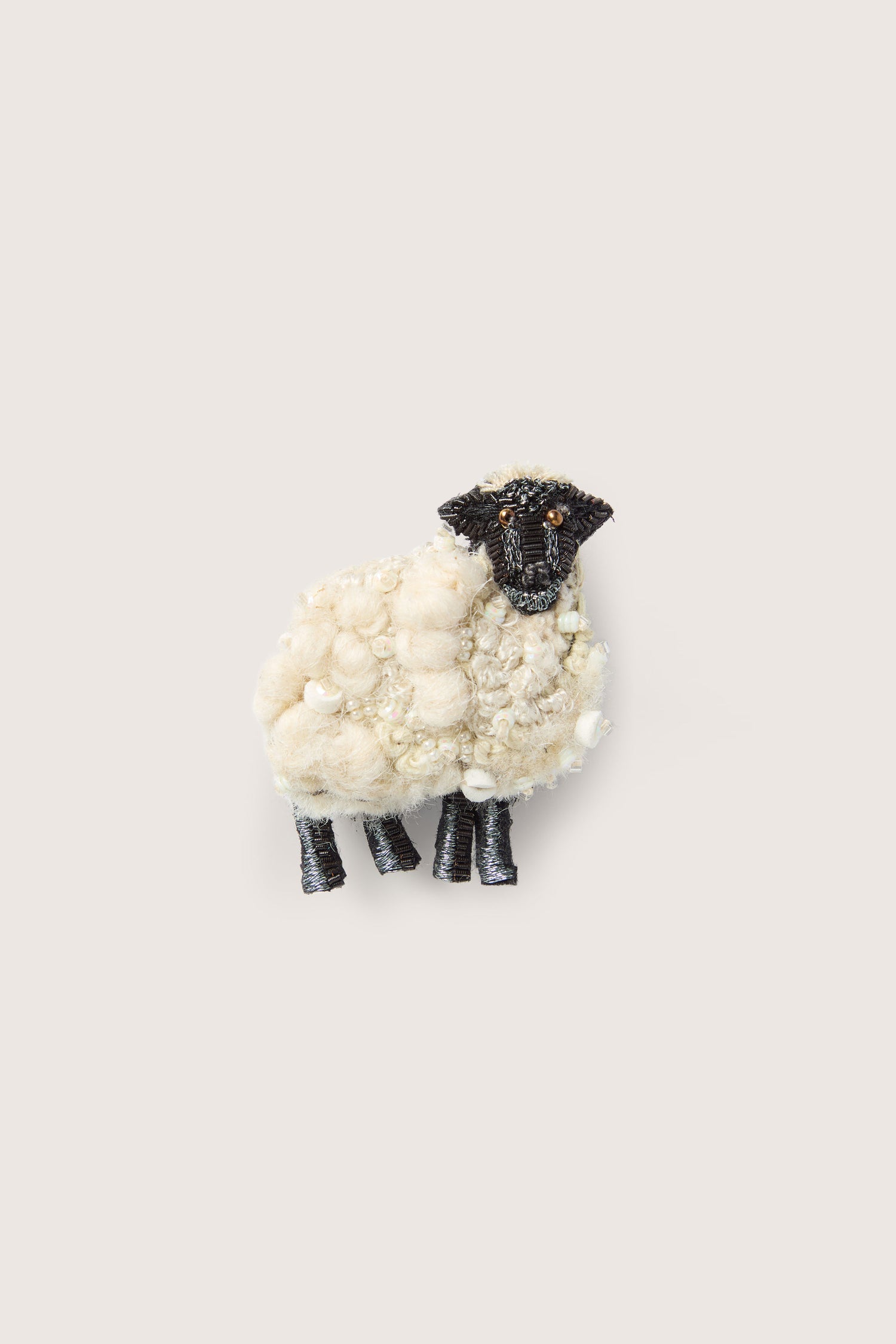 A small "Hand Embroidered Ewe Brooch" with a fluffy white body and black head and legs, perfect for adding charm to any ensemble, resembling the intricate detail of a Trovelore handcrafted brooch.