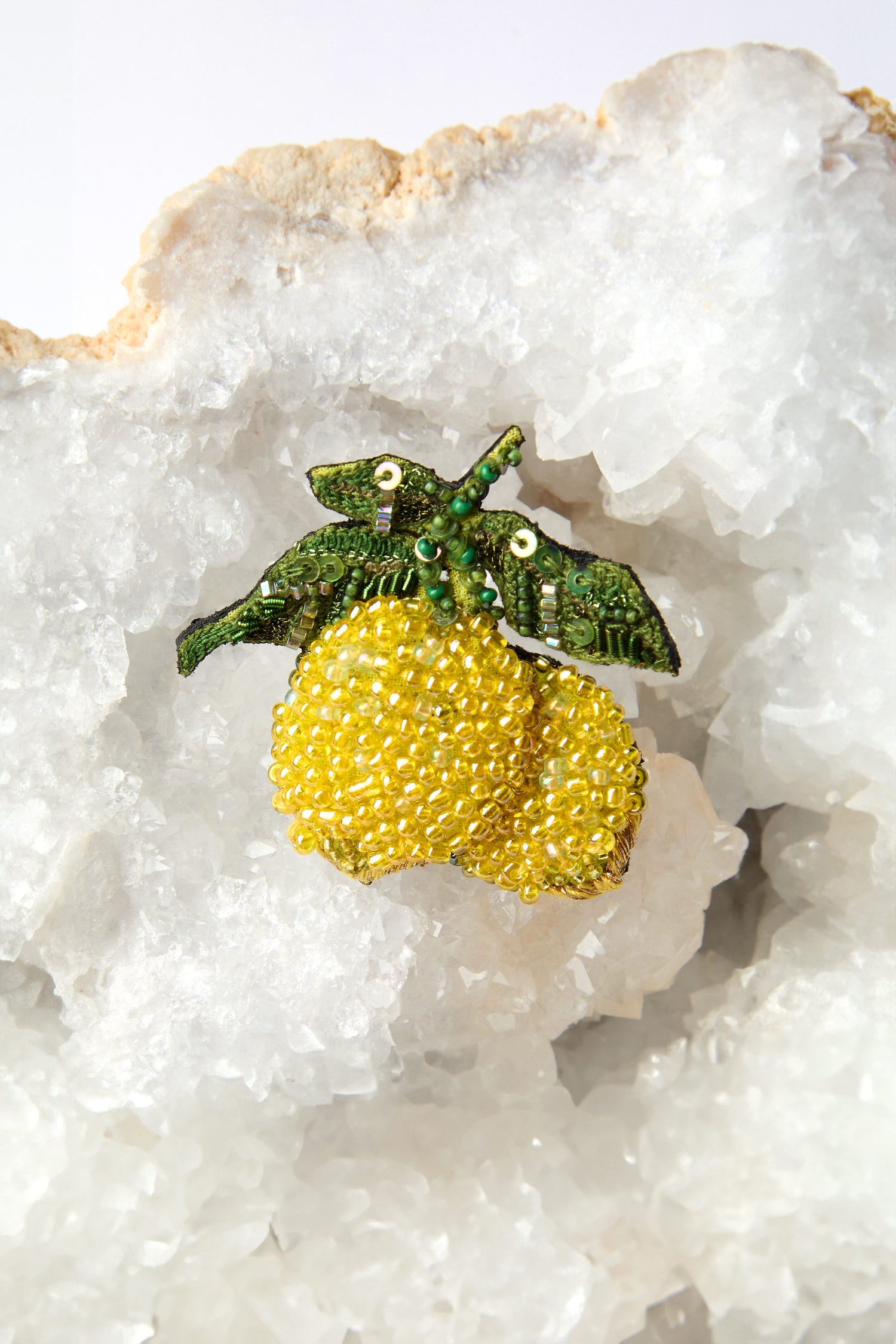 The Hand Beaded Amalfi Lemons Brooch, featuring vibrant green leaves on a white crystalline rock surface, beautifully captures the essence of Mediterranean charm in every bead.