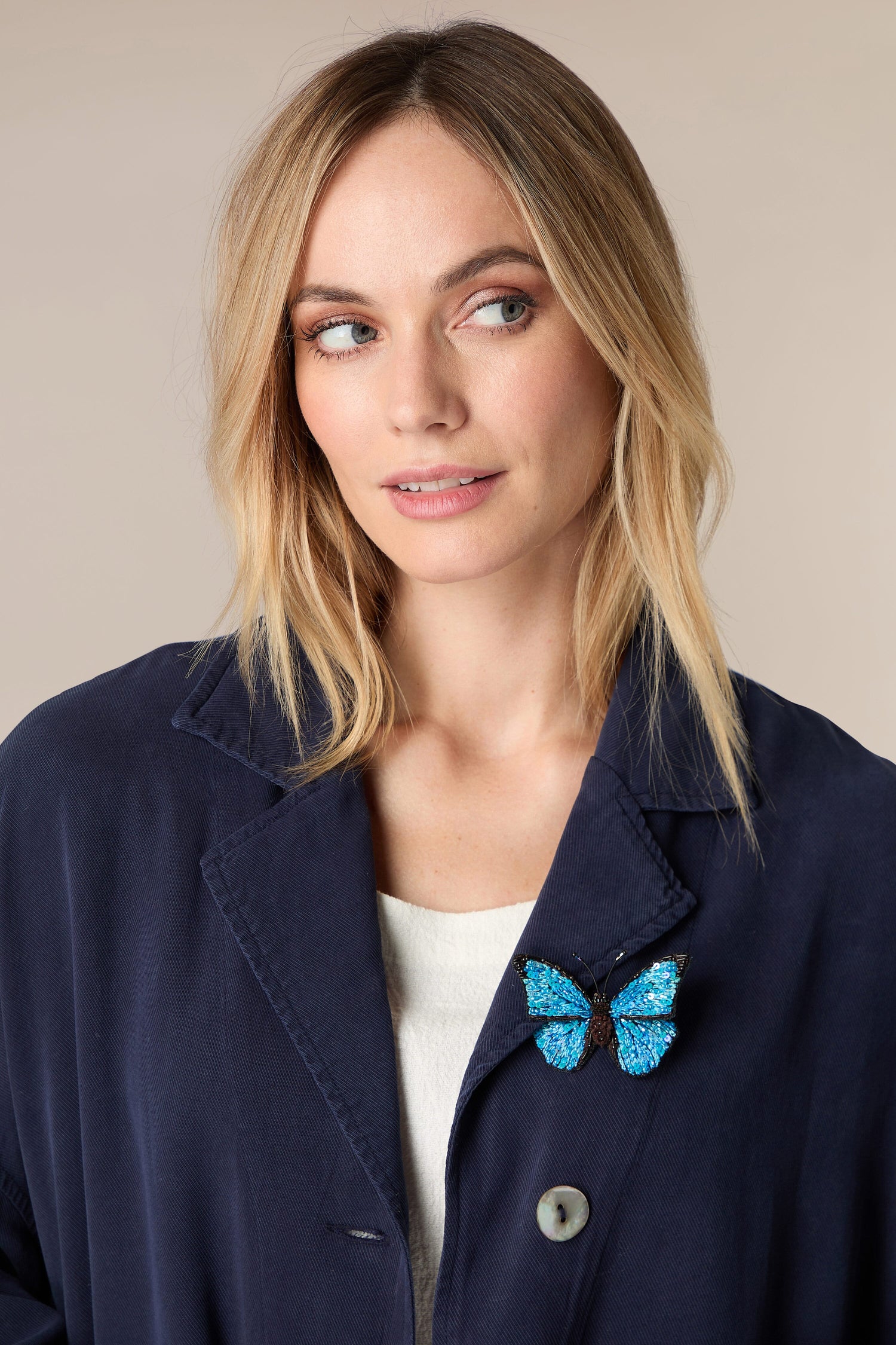 A woman wearing a whimsical blue jacket adorned with a Hand Embroidered Morpho Butterfly Brooch.