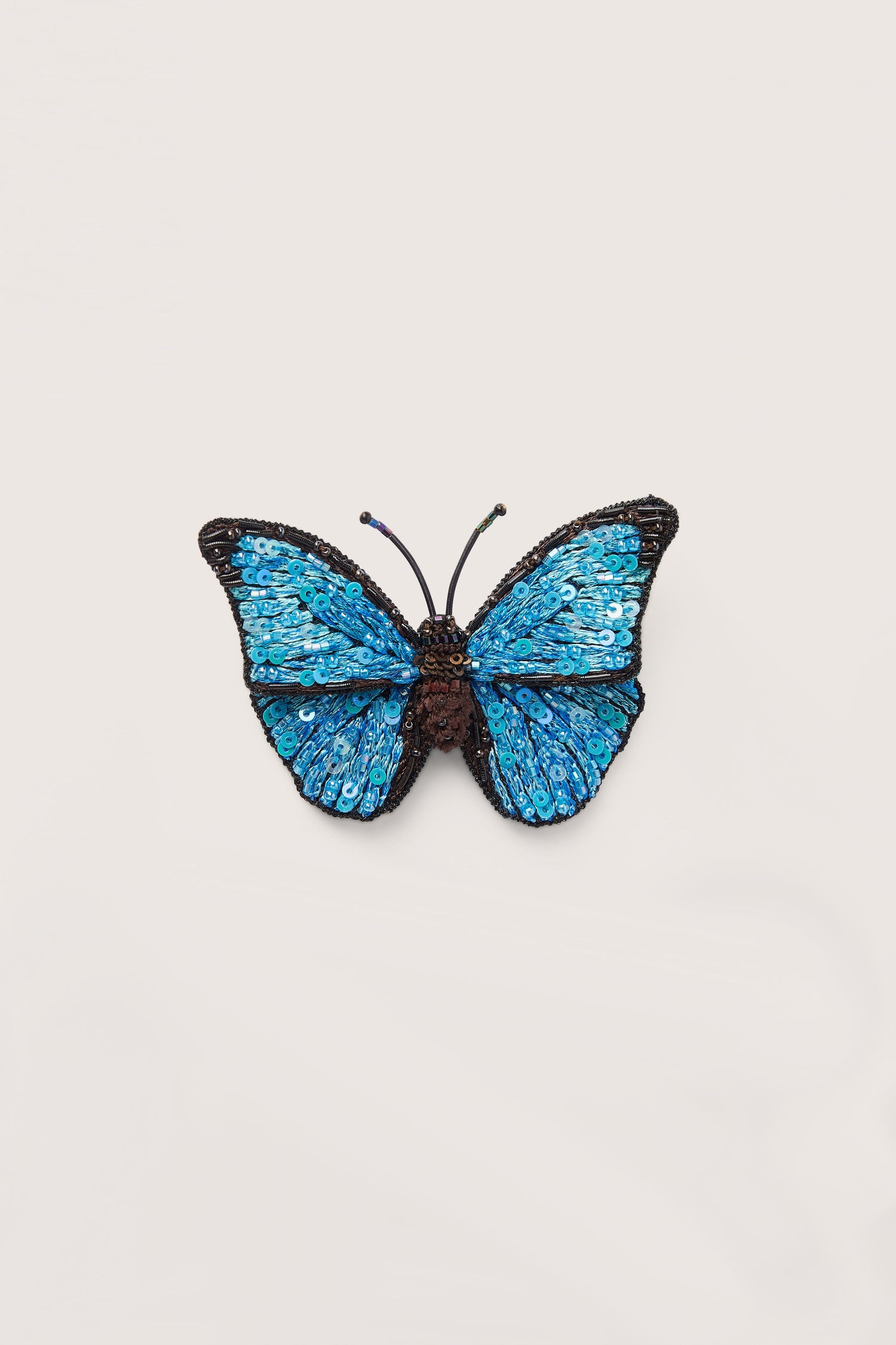 A hand embroidered Morpho butterfly brooch on a white background.