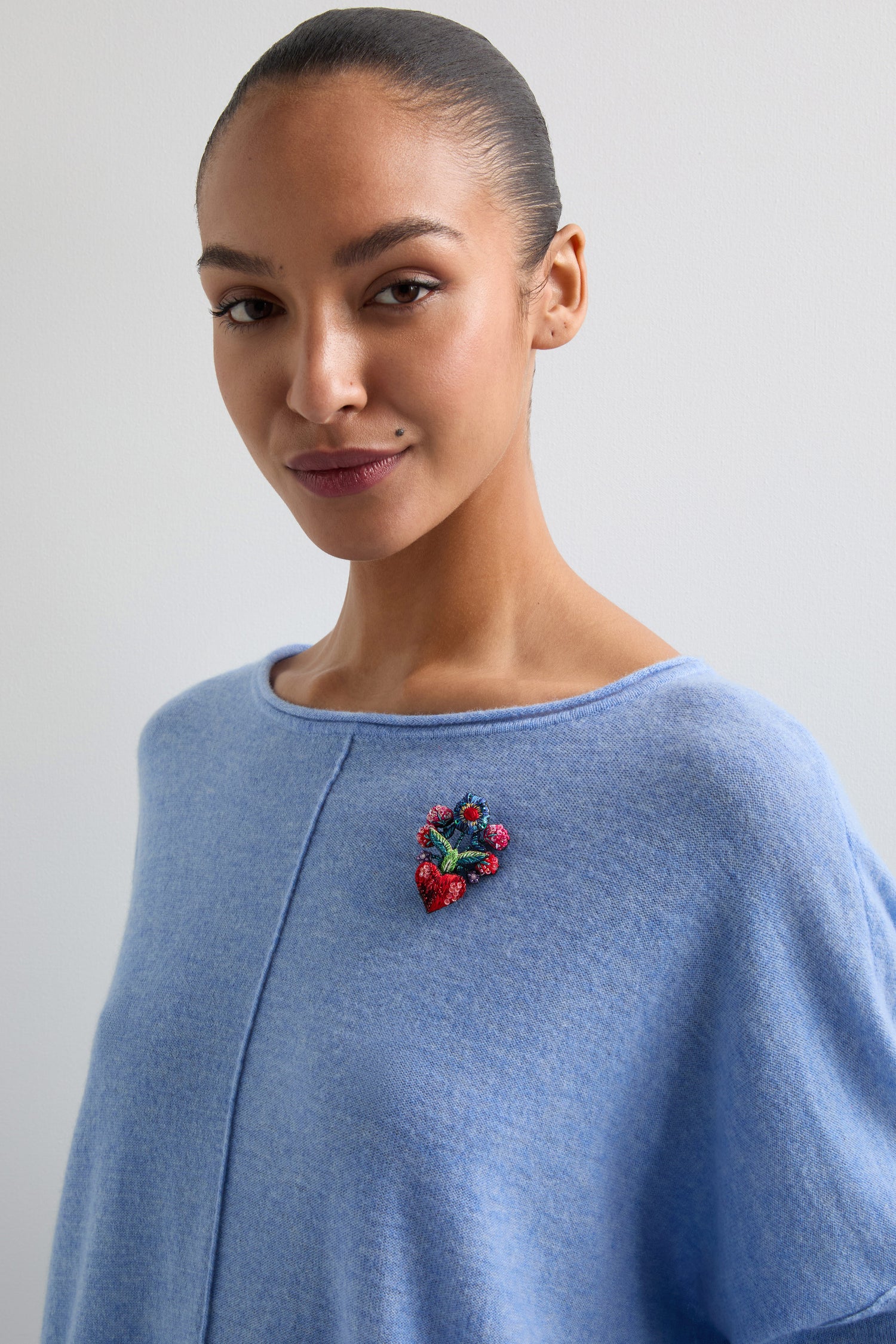 A person in a light blue top adorned with a Hand Beaded Flower Bouquet Brooch stands gracefully against a plain background.