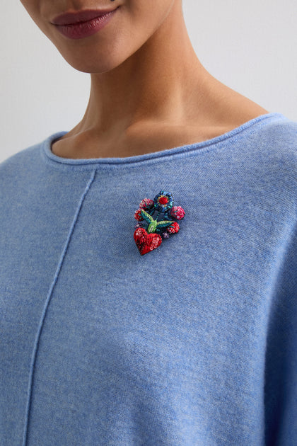 A person wearing a light blue top adorned with the stunning Hand Beaded Flower Bouquet Brooch by Trovelore, showcasing a burst of colorful floral charm near the shoulder.