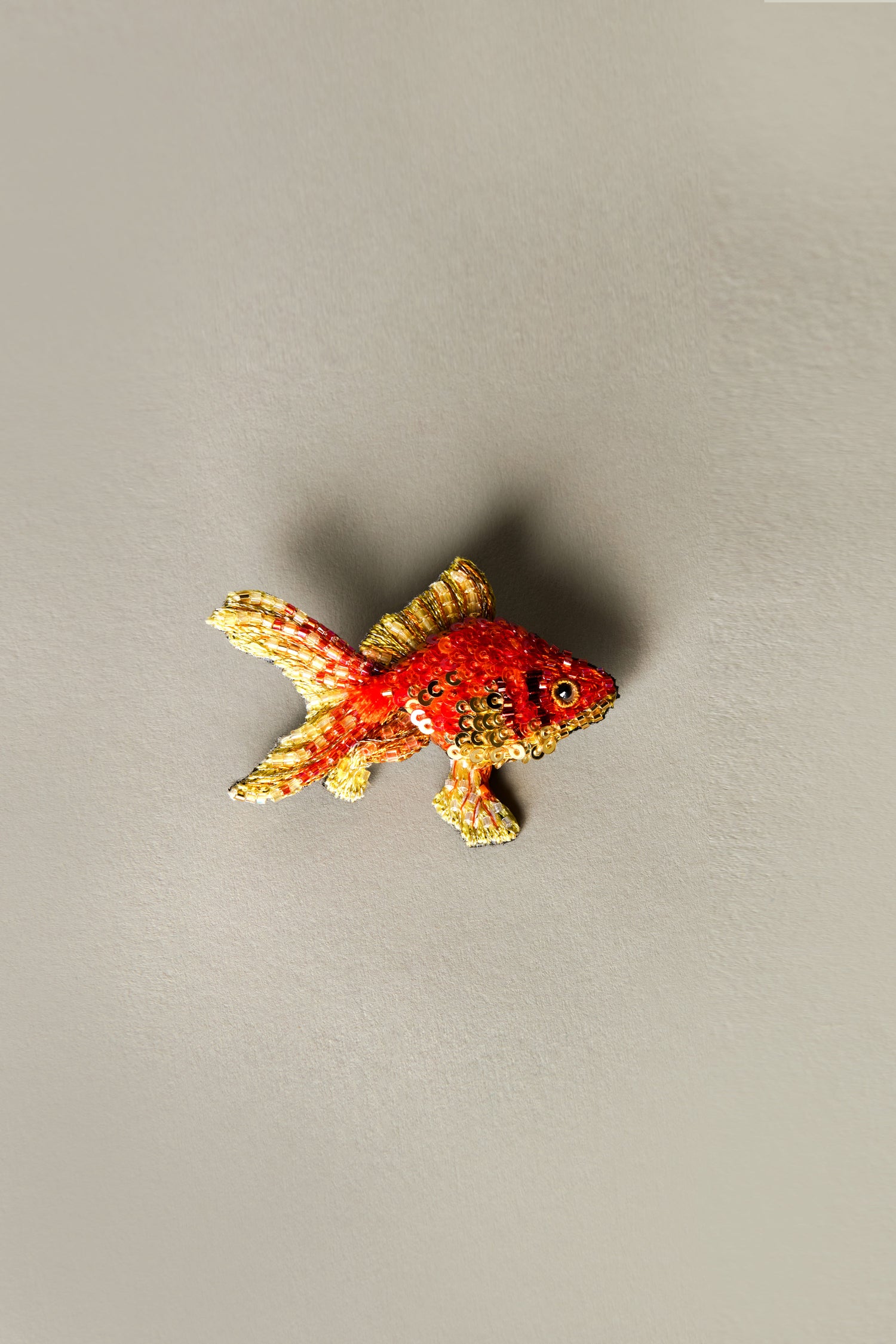 The Trovelore Hand Beaded Fantail Goldfish Brooch is exquisitely handcrafted, with intricate red and orange details on a subtle light gray background.