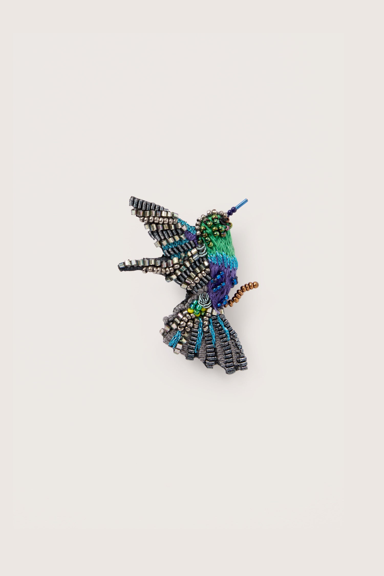 A sparkling crowned woodnymph embroidered brooch of a woodnymph hummingbird on a white surface.