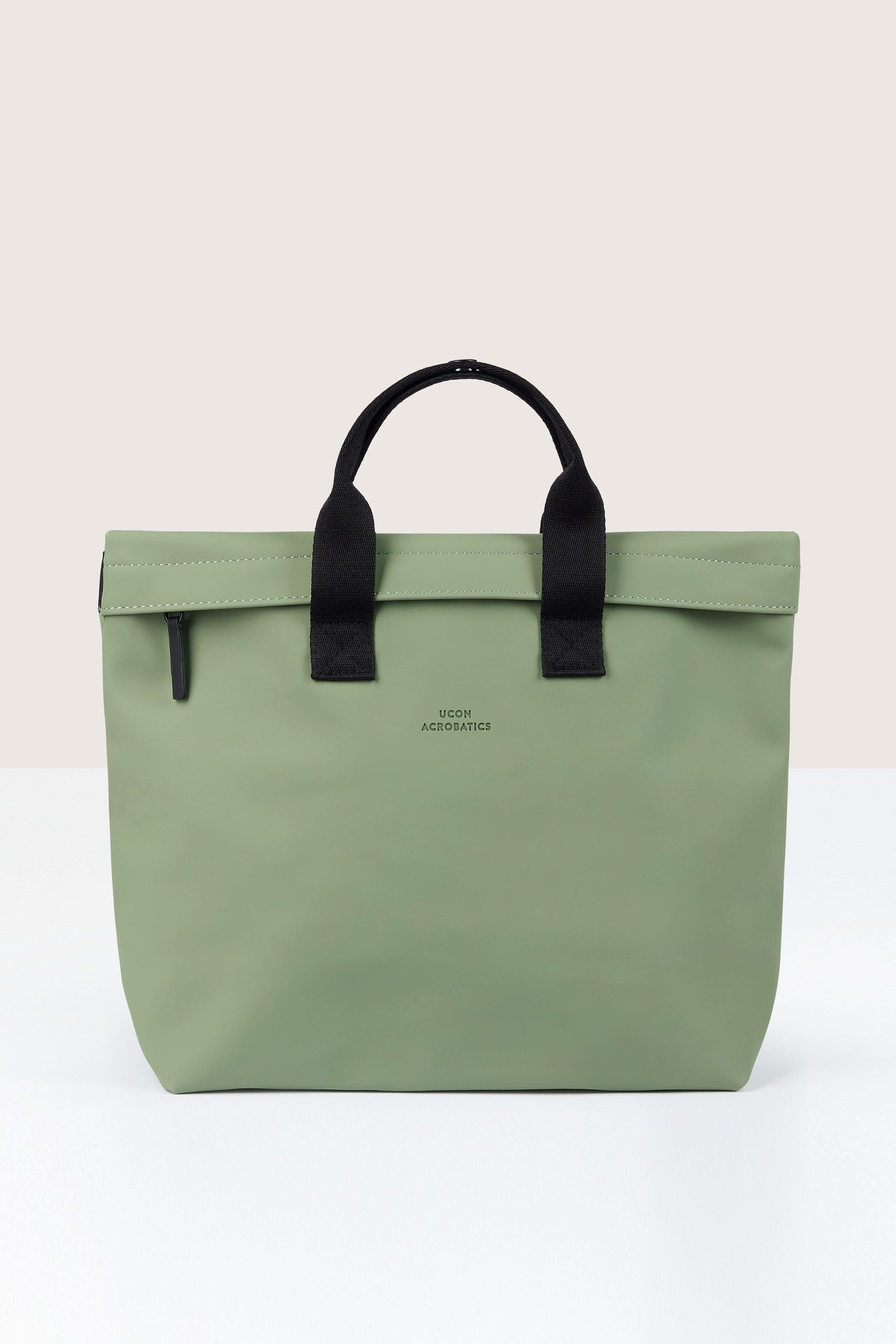 A light green tote bag with black handles and a zipper closure, labeled "Ucon Acrobatics" in small black text on the front. Crafted with a functional design reminiscent of the Eliza Roll Top Backpack, this eco-friendly accessory is made from recycled PET bottles.