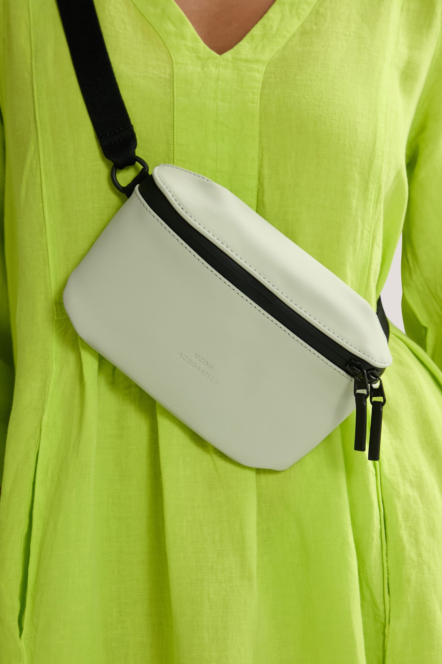 A person in a lime green dress wearing a water-repellent, white Jona Crossbody Bag with black zippers.