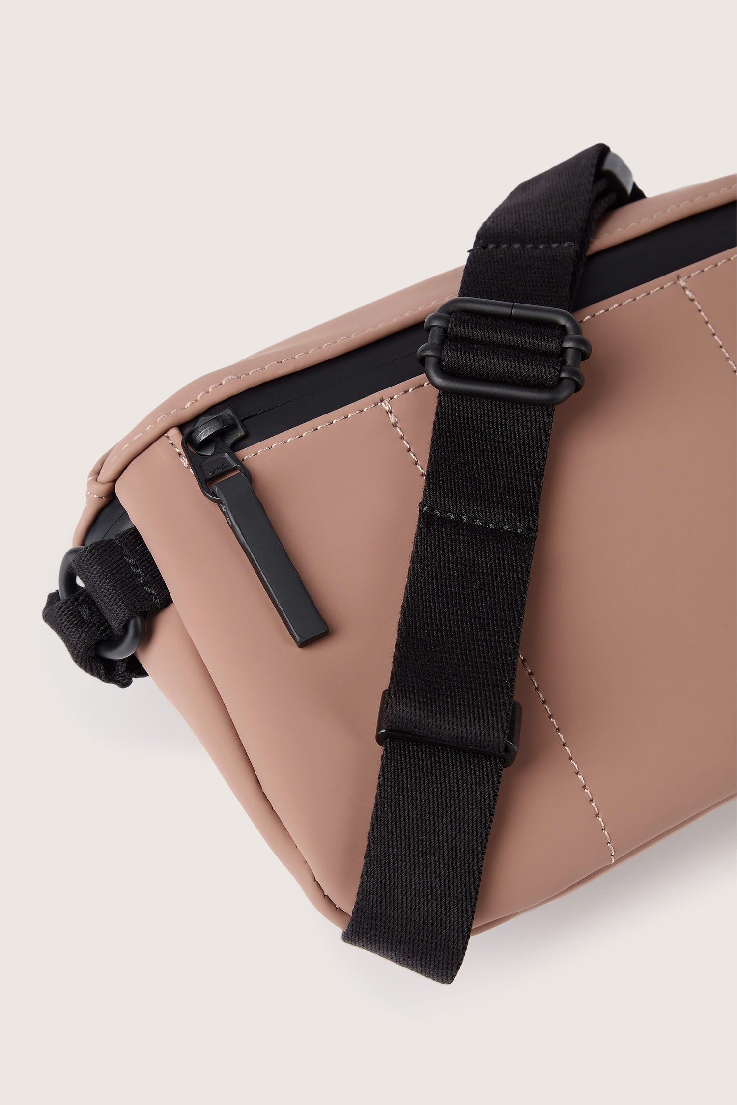 Close-up view of a beige Jona Crossbody Bag crafted from water-repellent, vegan tech material, featuring black adjustable straps and a sleek black zipper.