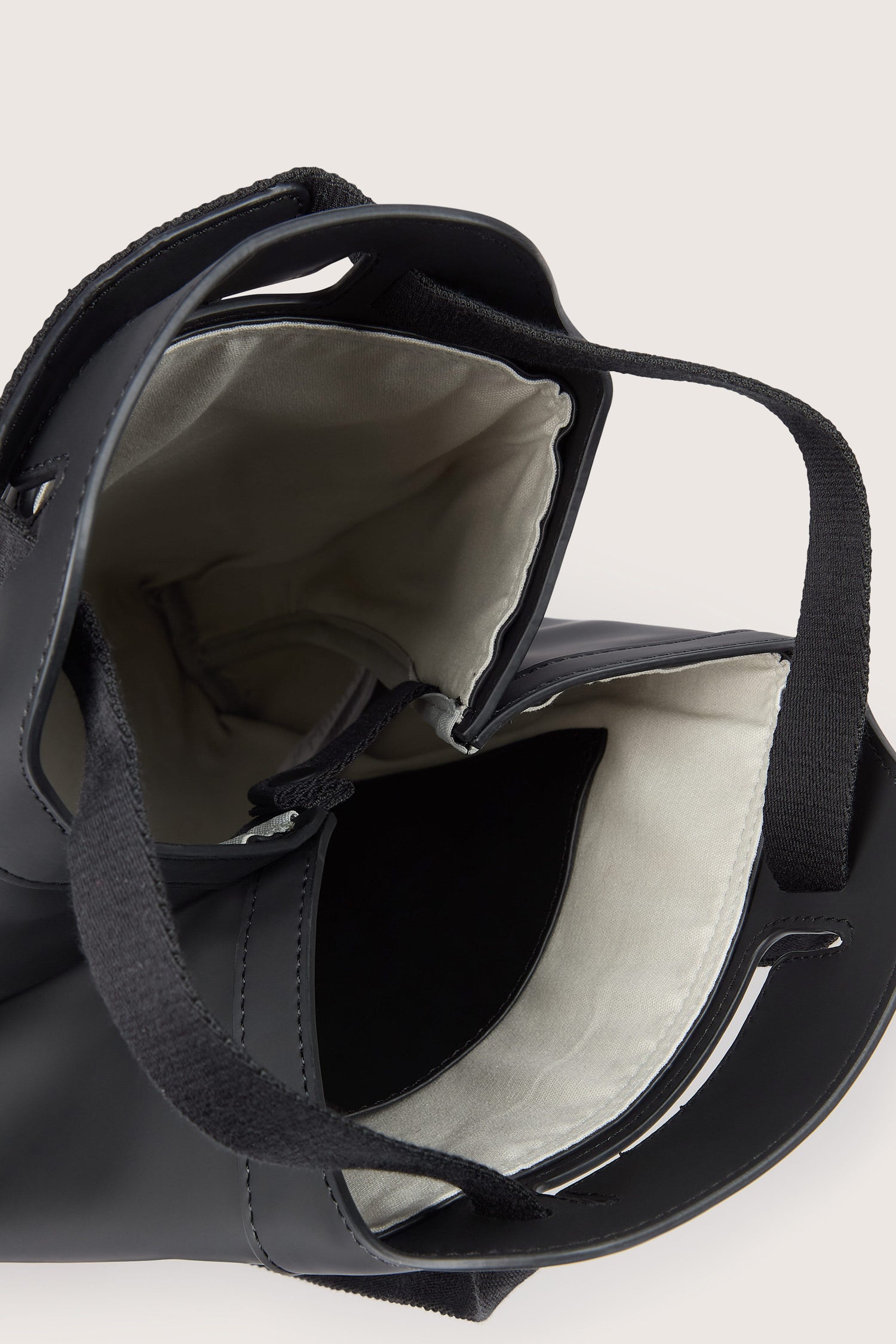 A black Una Backpack with a beige interior and two wide black handles is shown facing upwards, revealing its spacious inner compartment and versatile design.