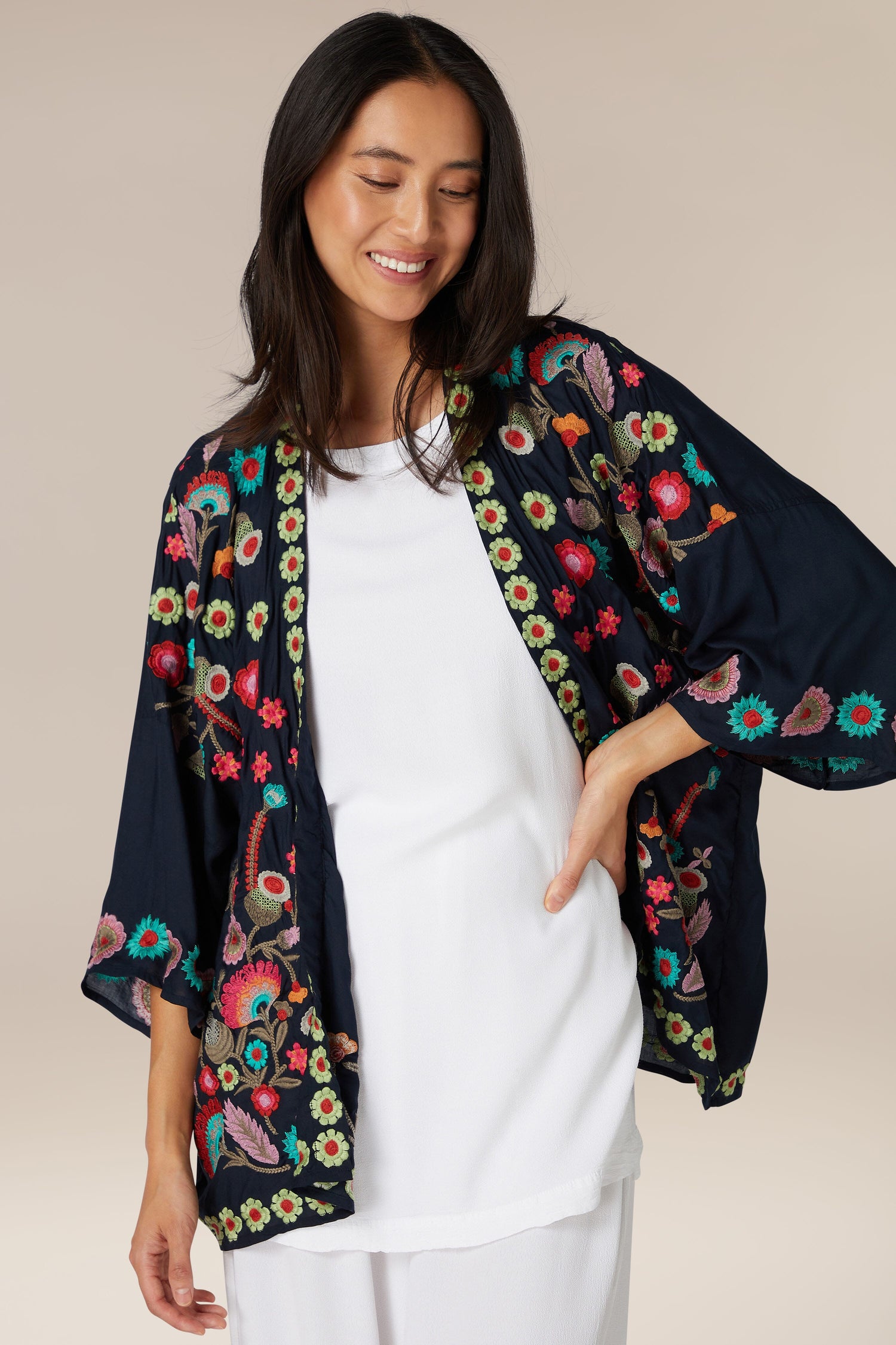 A woman smiling gently while posing in a white top and the Embroidered Flower Garden Kimono.