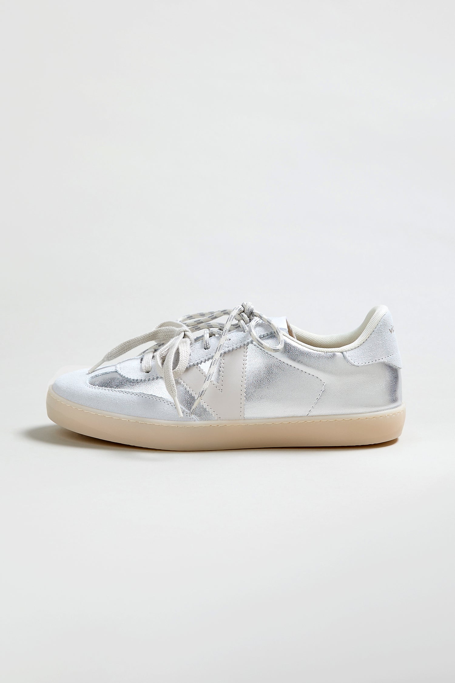 The Berlin Metallic Trainers are silver low-top sneakers with white laces, a white heel tab, and a light beige rubber sole, displayed against a plain light background.