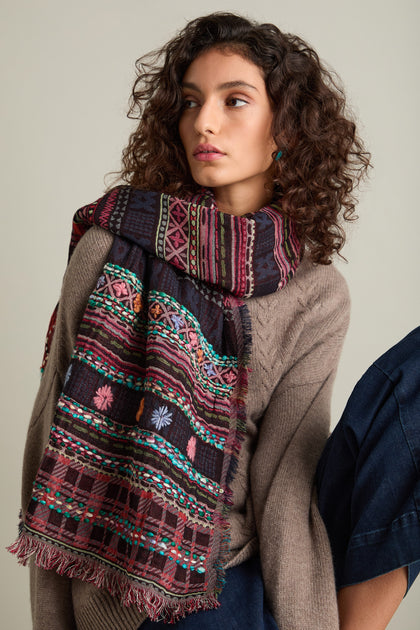 A woman with curly hair, dressed in a beige sweater and an exquisite Hand Embroidered Cotton Scarf, looks to the side against a plain background.