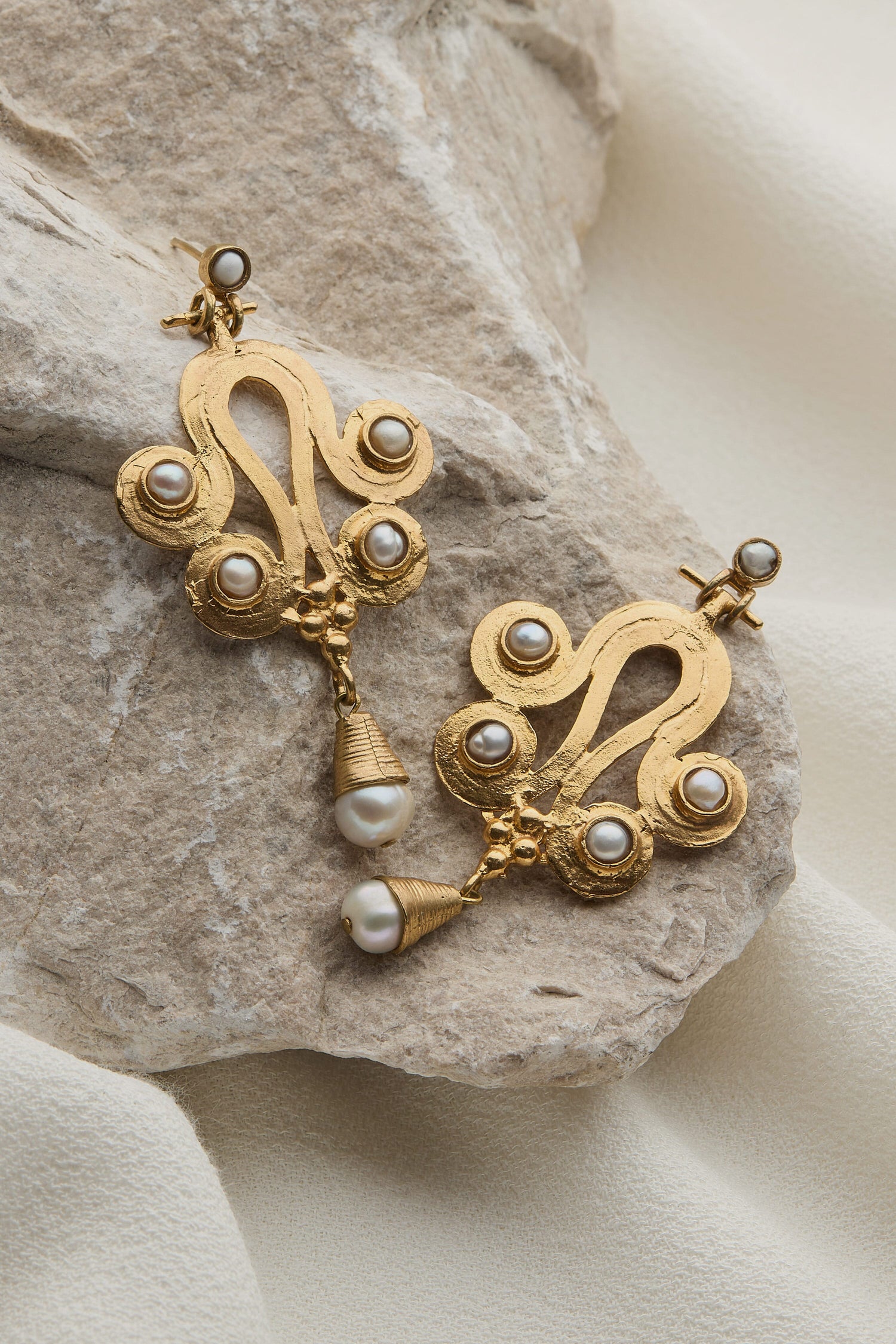 A pair of Handcrafted Ottoman Earrings with pearls on a rock.