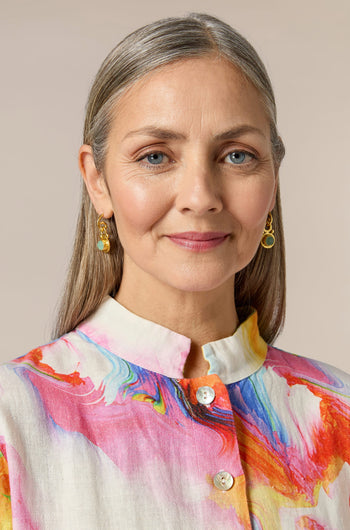 A woman wearing the Handcrafted Aquamarine Drop Earrings in Istanbul, elevating her colorful shirt and overall appearance with their stunning design.