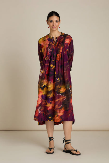 A woman stands wearing an Abstract Flower Pleated Dress with black sandals against a plain background, evoking the vibrant essence of impressionist art.