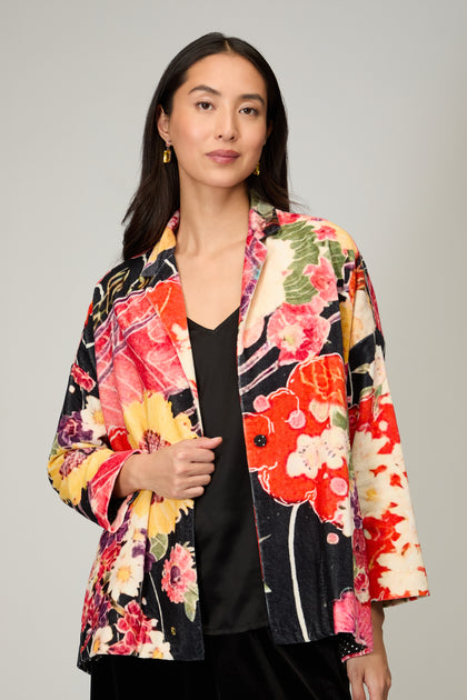 A woman wearing the Abstract Poppy Velvet Jacket over a black top stands against a plain light gray background.