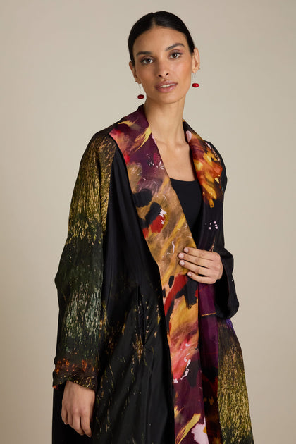 A woman wearing a Reversible Abstract Flower Print Jacket over a black top stands against a neutral background, exuding artful elegance as she looks at the camera.