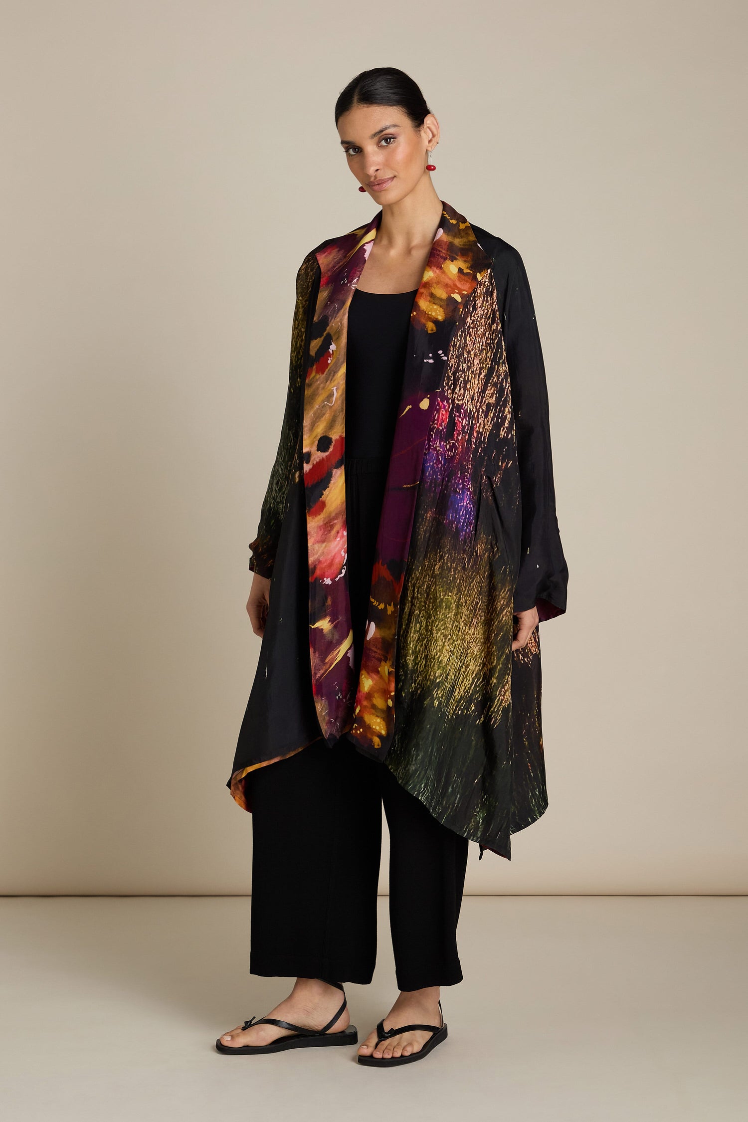 The sentence already contains the product name "Reversible Abstract Flower Print Jacket." Therefore, no replacement is needed. Here's the original sentence for reference:

"A person stands against a plain background, exuding artful elegance in a Reversible Abstract Flower Print Jacket over a black top and pants, with relaxed silhouette accentuated by black sandals.