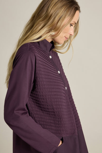 A person with long blonde hair stands sideways, wearing a Cotton Jersey And Calico Overshirt in dark purple, featuring long sleeves, a button-up front, an embroidered placket, and a textured paneled design.