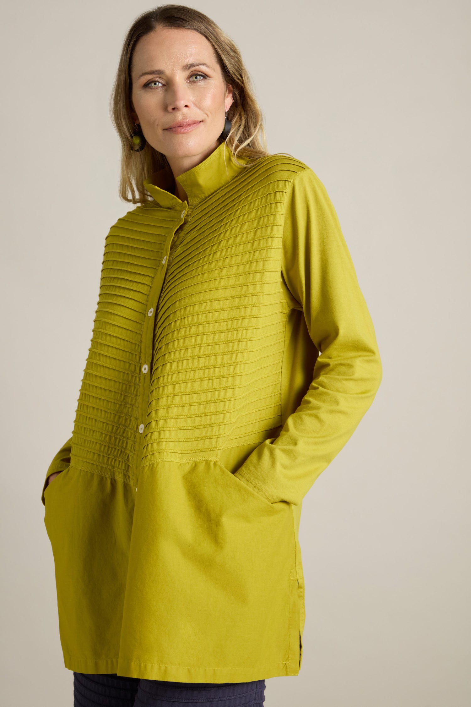 A woman wearing the Cotton Jersey And Calico Overshirt in green, featuring long sleeves, button-up front, textured detailing, and an embroidered placket looks at the camera with her hands in her pockets.