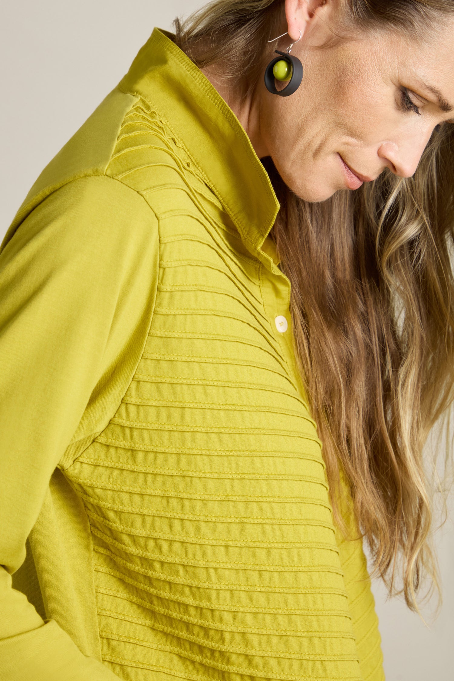 A woman with long hair looks down while wearing a brightly colored Cotton Jersey And Calico Overshirt and circular earrings.