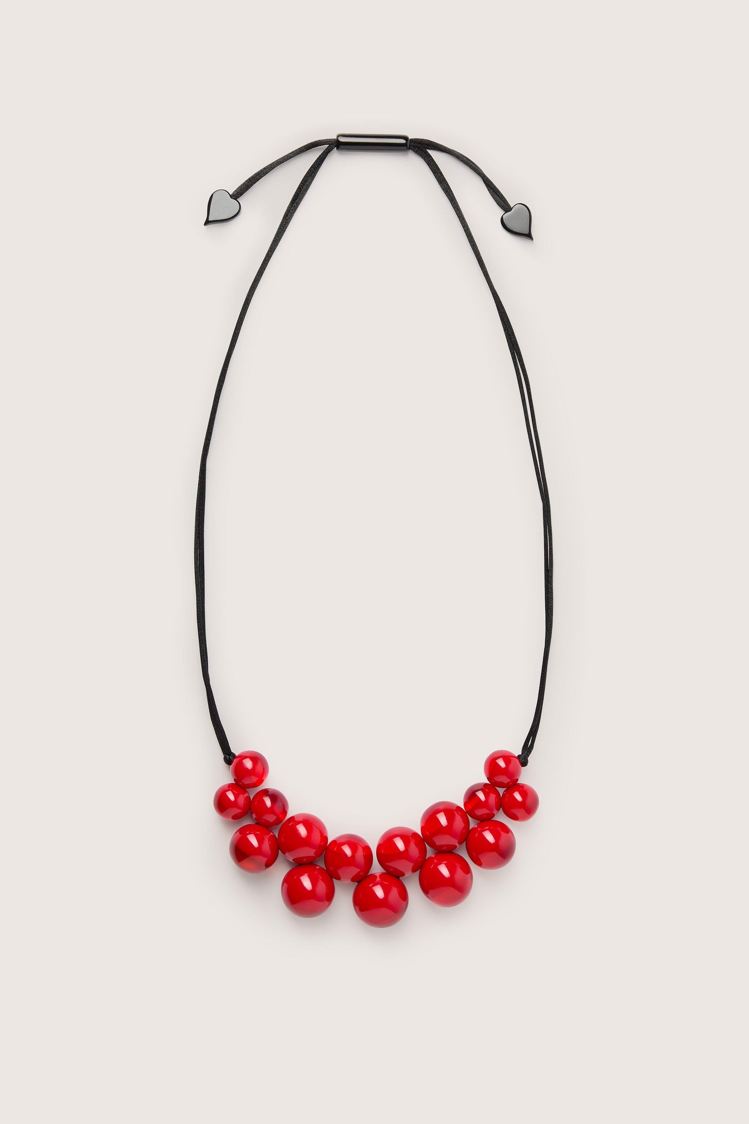 A handmade Spheres Necklace with a red pendant on a black cord.