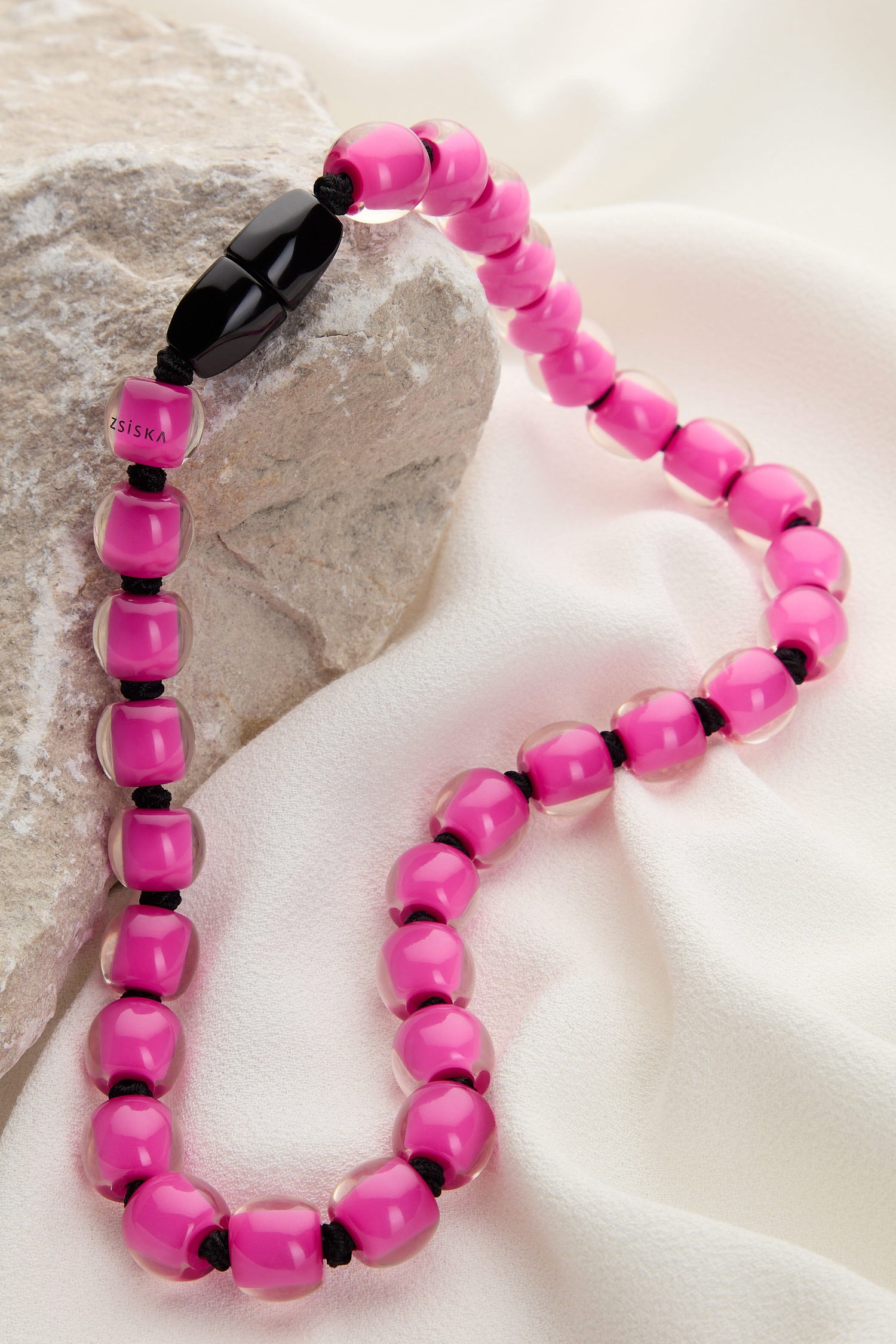 A Colourful Beads Necklace with black accents arranged on a beige cloth and stone surface. The glossy, colourful beads are strung together on a black cord.