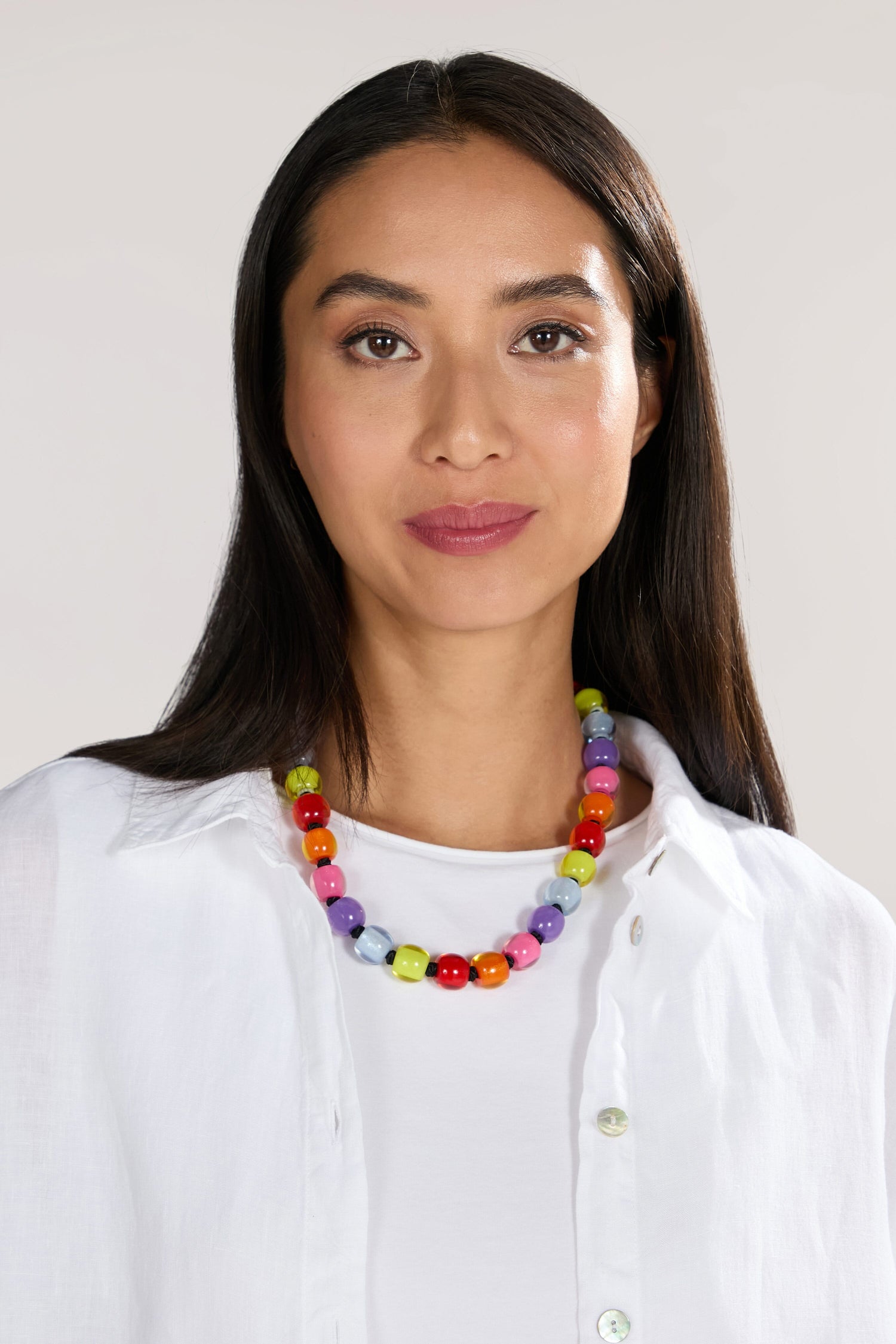 Woman with long dark hair wearing a white shirt and a Colourful Beads Necklace, looking directly at the camera.