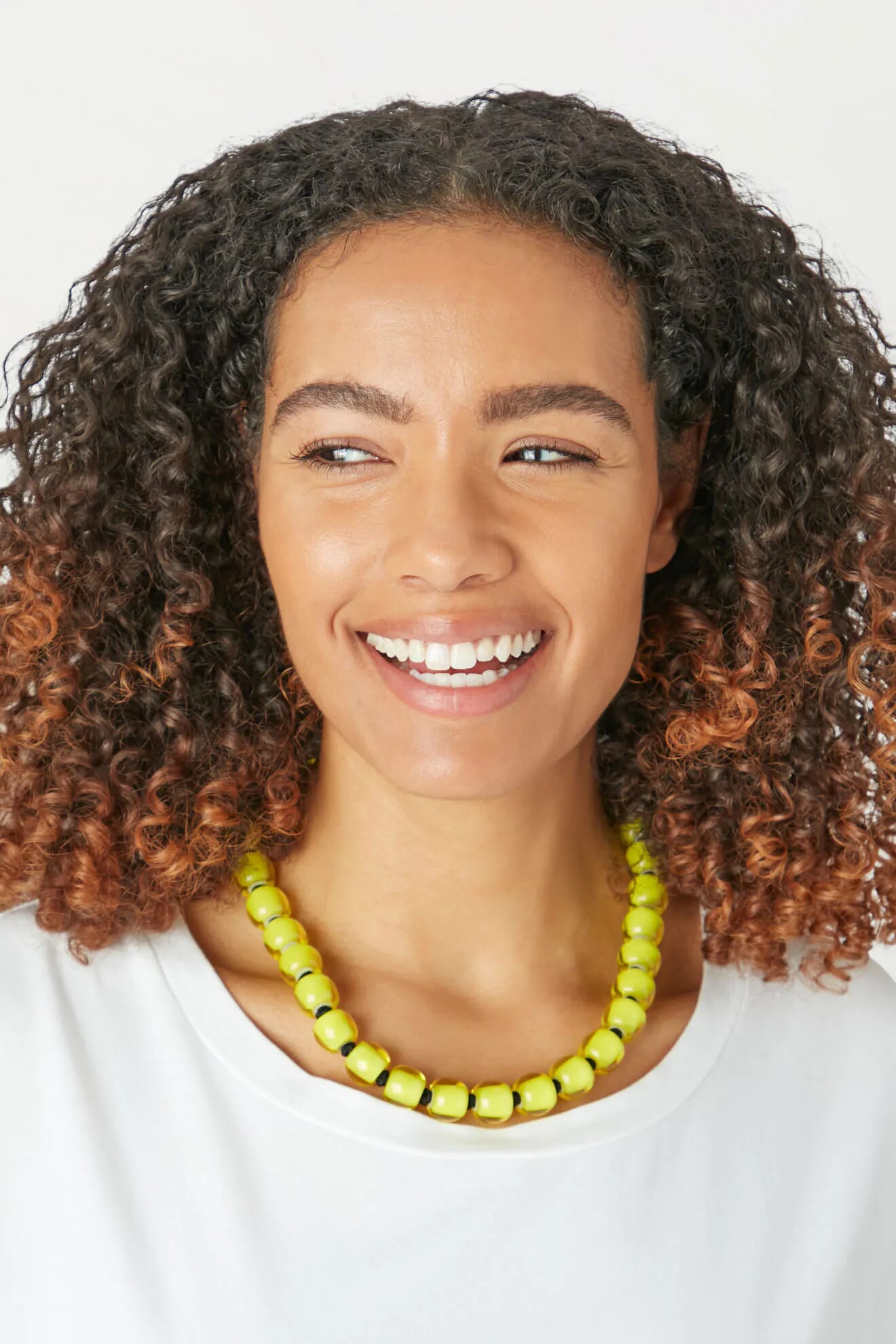 A young woman with curly hair wearing a Colourful Bead Necklace in the quirky world.