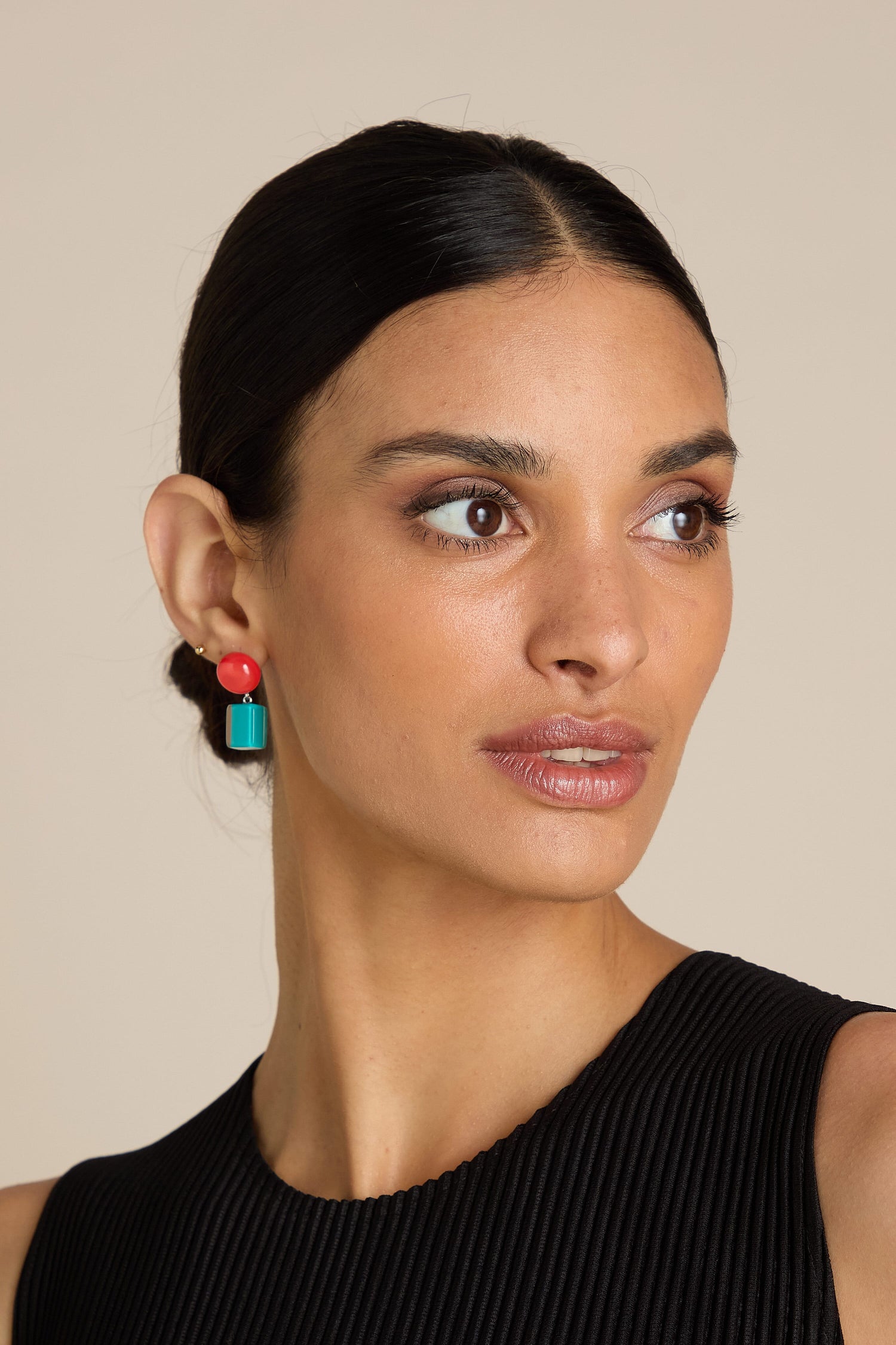 Woman with dark hair in an updo, wearing colorful Sphere and Cube Resin Earrings and a black sleeveless top, looking to her left against a neutral background.