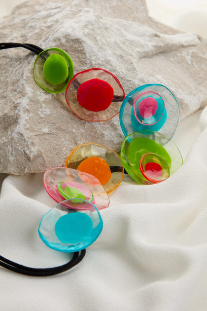 Colorful translucent plastic Resin Flower Necklace in various bright colors is arranged on a white fabric and a light-colored rock, evoking the vibrant charm of an abstract piece.