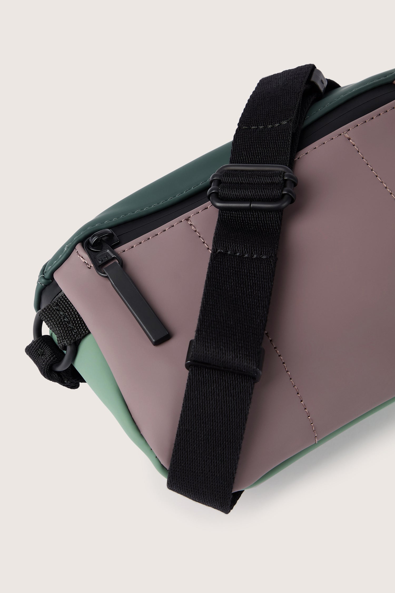 Close-up of the Jona Crossbody Bag with green and mauve panels, featuring a black adjustable strap and a zipper closure, crafted from water-repellent vegan tech material.